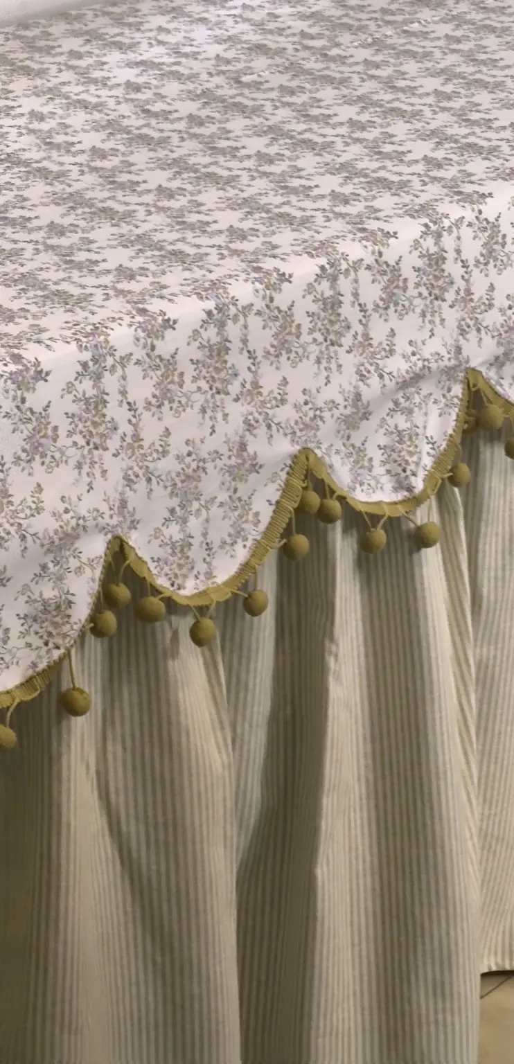Detalhe da sobretoalha floral Onda com pom-pom sobre base em linho alentejano pistache