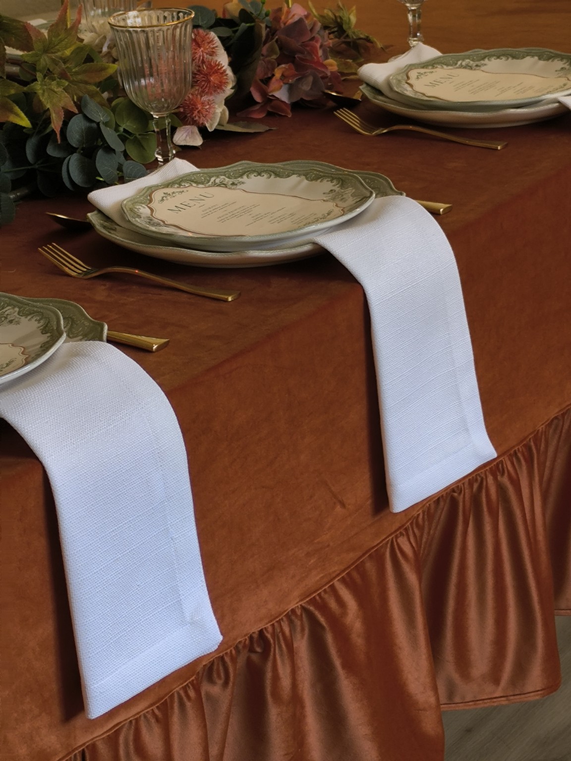 Guardanapos brancos numa mesa posta com toalha terracota e loiça verde